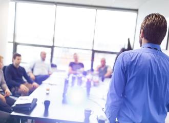 A corporate training is standing in front of a group of people seated at a table