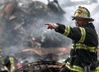 fire fighter standing in building rubble with full protective clothing on, shouting and pointing to the left
