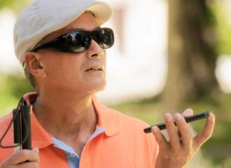 Vision impaired man holding long cane in one hand and mobile phone in the other hand