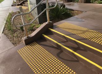Yellow stair tread nosing strips on wet concrete, with yellow discrete tactile indicators on both stair landings