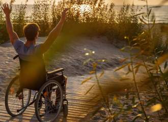 Young man using a wheelchair relaxing on the beach over sunset