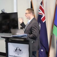 Lee Wilson speaking at a government conference, in front of the national flags
